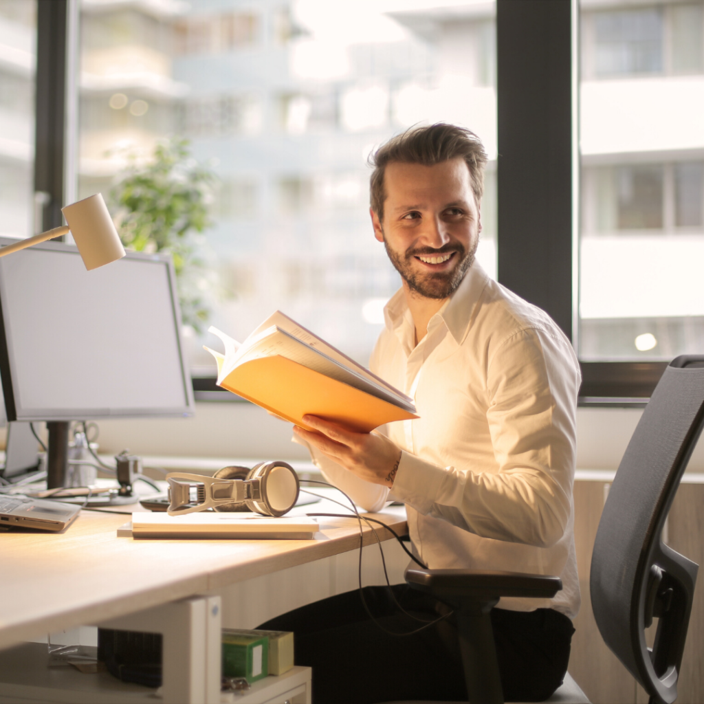 Employee Appreciation | a smiling man in a white shirt holding a yellow book in a working office