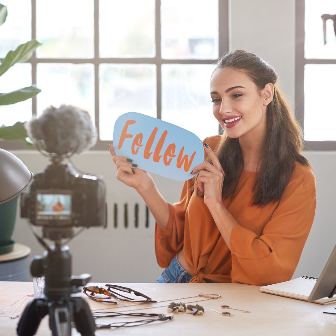 influencer marketing a woman sat in her office smiling at a camera and holding a sign saying follow
